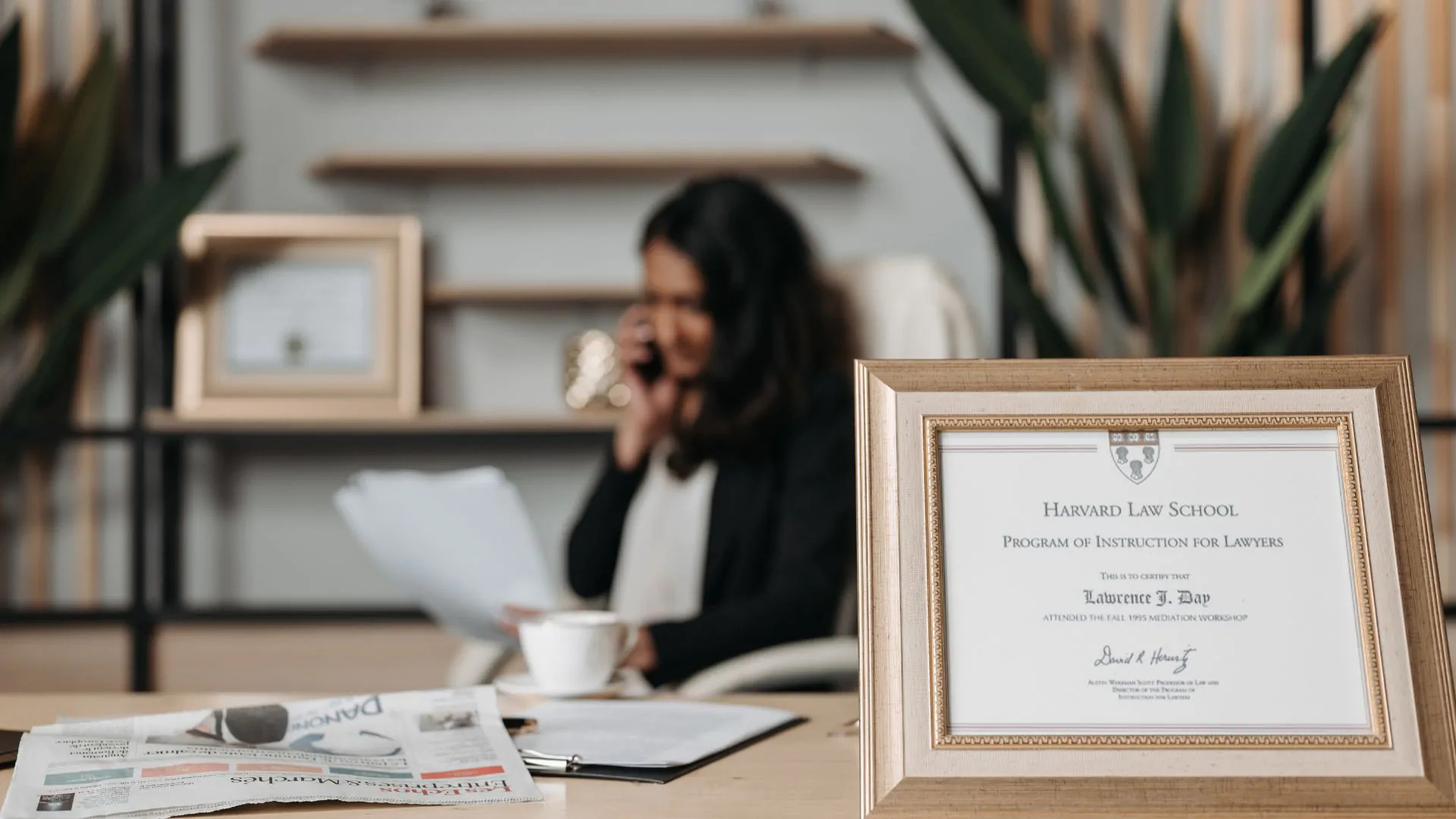 professional business woman sitting at desk with gold framed diploma from harvard law school next to her certificate of college degree