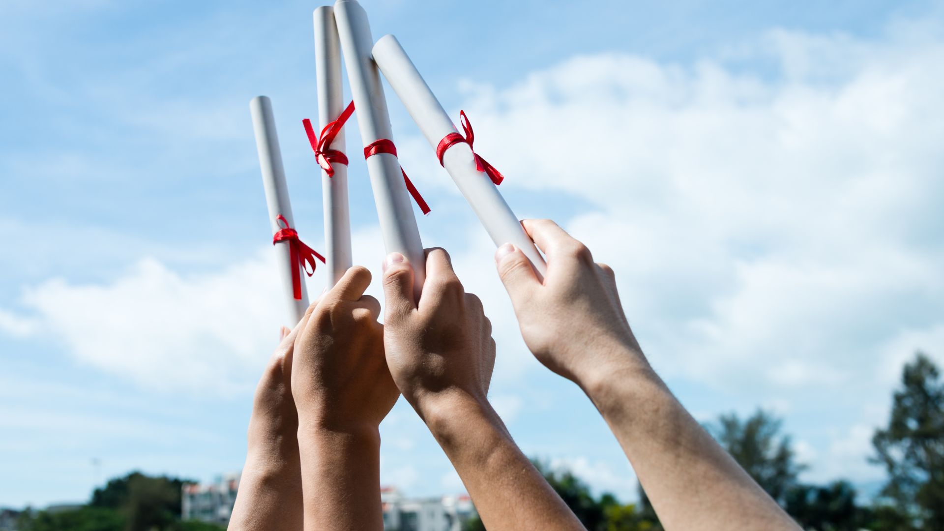 Step-By-Step Guide on How to Obtain a College Diploma Replacement 2 students holding replacement college diplomas up in the air against a beautiful blue sky